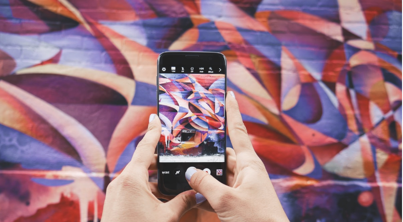 Picture of a woman using a large screen phone to take a picture of a mural